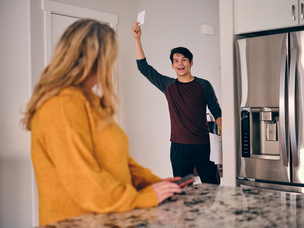 Boy with red and black shirt holding up a piece of mail